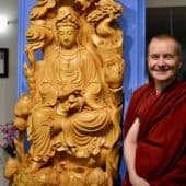 Venerable Sangye Khadro stands next to a wooden statue of Kuan Yin.