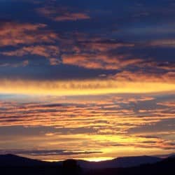 Orange streaks in a cloudy sky as the sun sets.