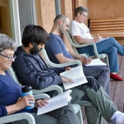 Four guests sit and read in chairs on the deck of Chenrezig Hall.