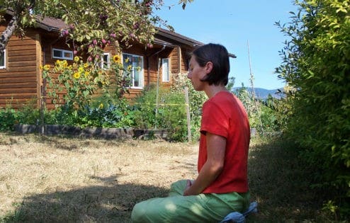 A young woman sits in meditation in the garden under a tree.