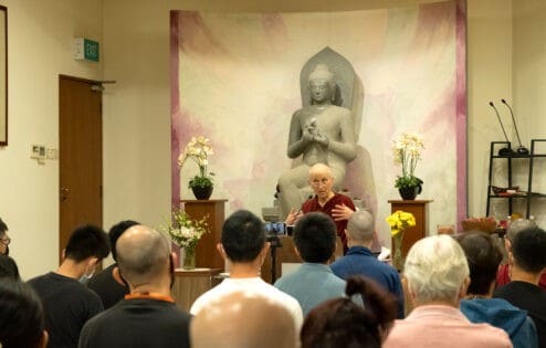 Venerable Chodron sitting in front of a large Buddha statue while teaching to a group of students.