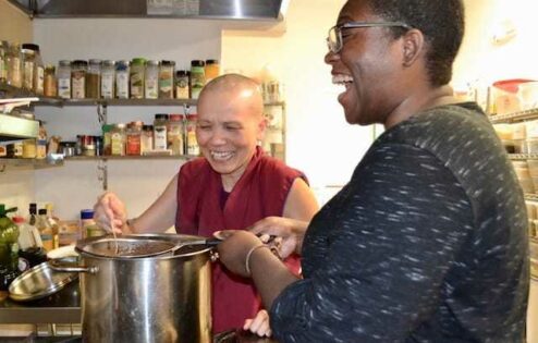 Rashika laughing while cooking in the Sravasti Abbey kitchen with Venerable Penne.