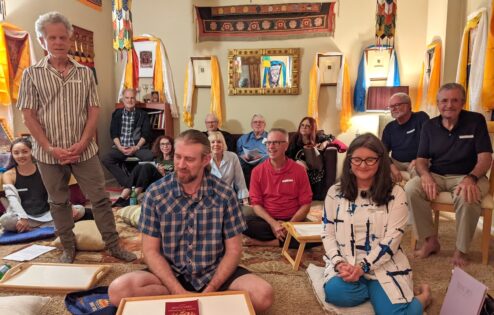 A group of people sitting in a room, surrounded by thangkas.