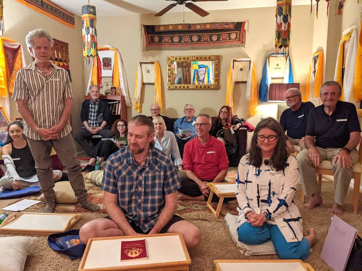 A group of people sitting in a room, surrounded by thangkas.