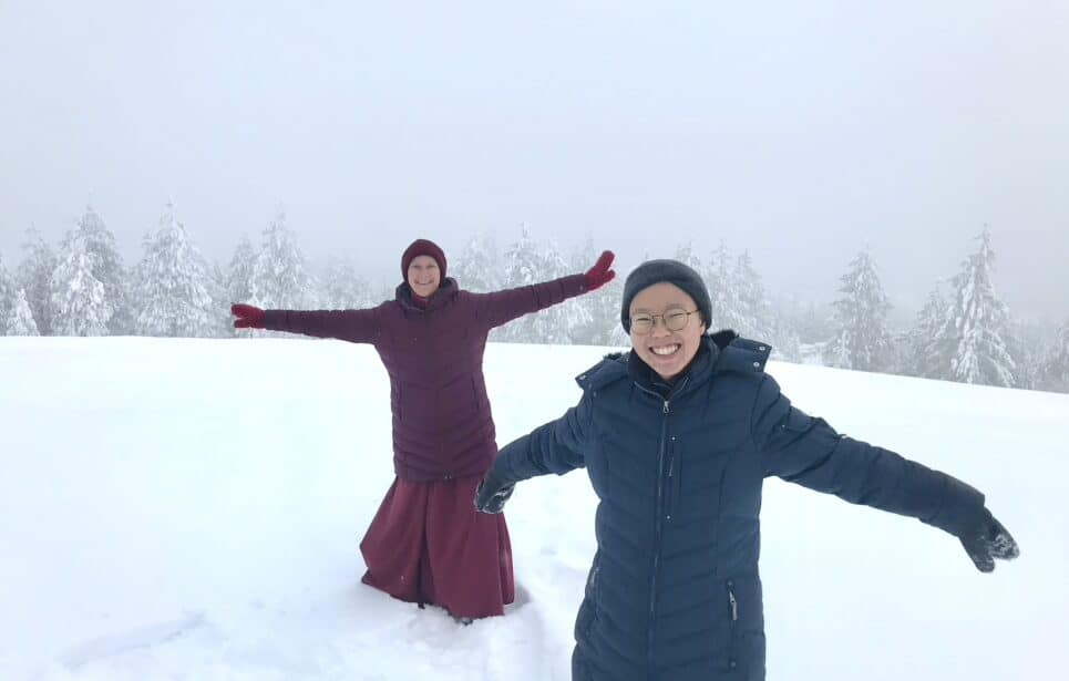 Dronsel and a monastic smiling with arms out, in a snowy meadow.