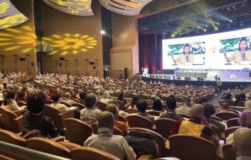 Group of people sitting in a crowded auditorium watching a presentation on a large screen.