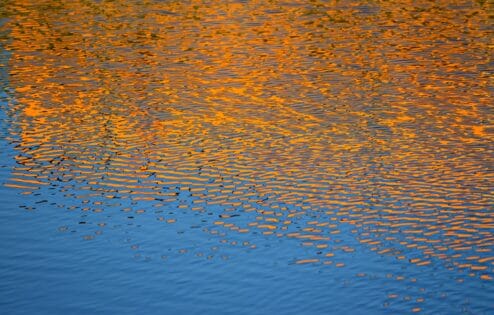 Orange sunset reflected in rippling water.