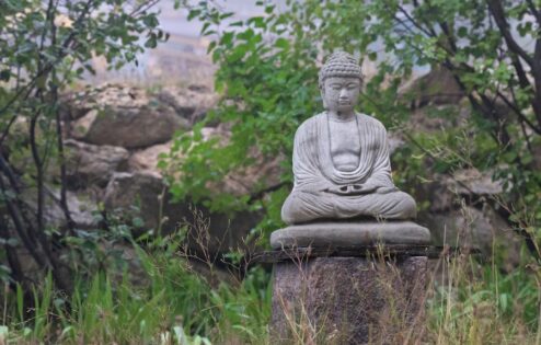 A stone Buddha statue in the garden on a pedestal.