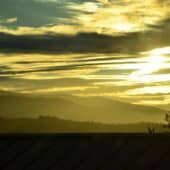 Sunlight appears through rows of clouds above hills.